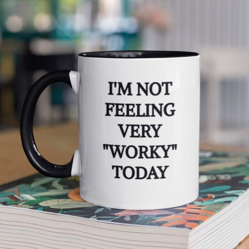 May include: White ceramic coffee mug with a black rim and handle. The mug has black text that reads "I'm not feeling very "worky" today."
