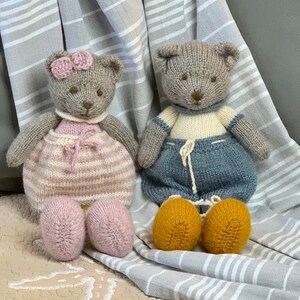 Könnte beinhalten: Zwei gestrickte Teddybären, einer in rosa und weißen Streifen und der andere in blauen und weißen Streifen. Beide Bären haben braune Augen und Nasen und sitzen auf einem gestreiften Stoff.