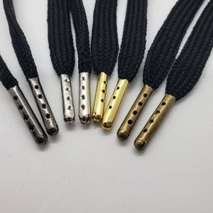 May include: A set of six black shoelaces with metal aglets in different finishes: silver, gold, and bronze. The aglets have a rounded end and five holes.