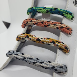 May include: White leather shoe with four different colored shoelaces. The shoelaces are black and white, black and orange, black and tan, and black, green, and blue.