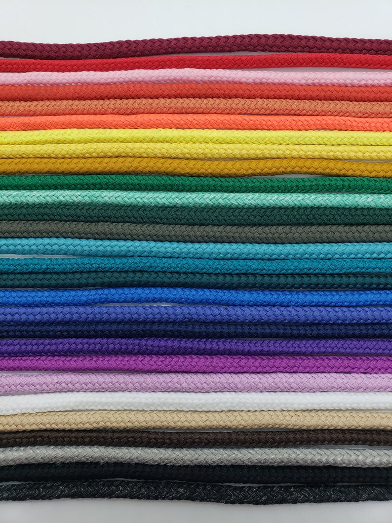 Op de afbeelding: Een verzameling van 20 verschillende gekleurde koorden, gerangschikt in rijen, tegen een witte achtergrond. De koorden zijn allemaal even dik en hebben dezelfde textuur, en ze zijn allemaal gemaakt van een geweven materiaal.