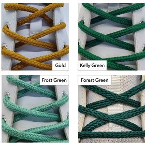 Op de afbeelding: Close-up van vier paar veters in verschillende kleuren: goud, kellygroen, vorstgroen en bosgroen. De veters zijn door de veterogen van een witte schoen geweven.