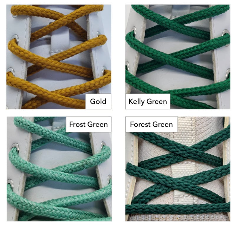 Op de afbeelding: Close-up van vier paar veters in verschillende kleuren: goud, kellygroen, vorstgroen en bosgroen. De veters zijn door de veterogen van een witte schoen geweven.