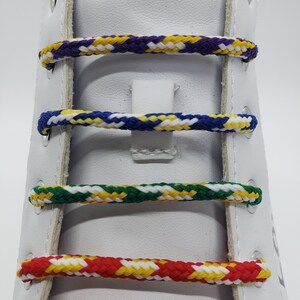 May include: Close-up of a white shoe with four different colored shoelaces. The shoelaces are braided and feature a mix of yellow, red, green, blue, and purple.