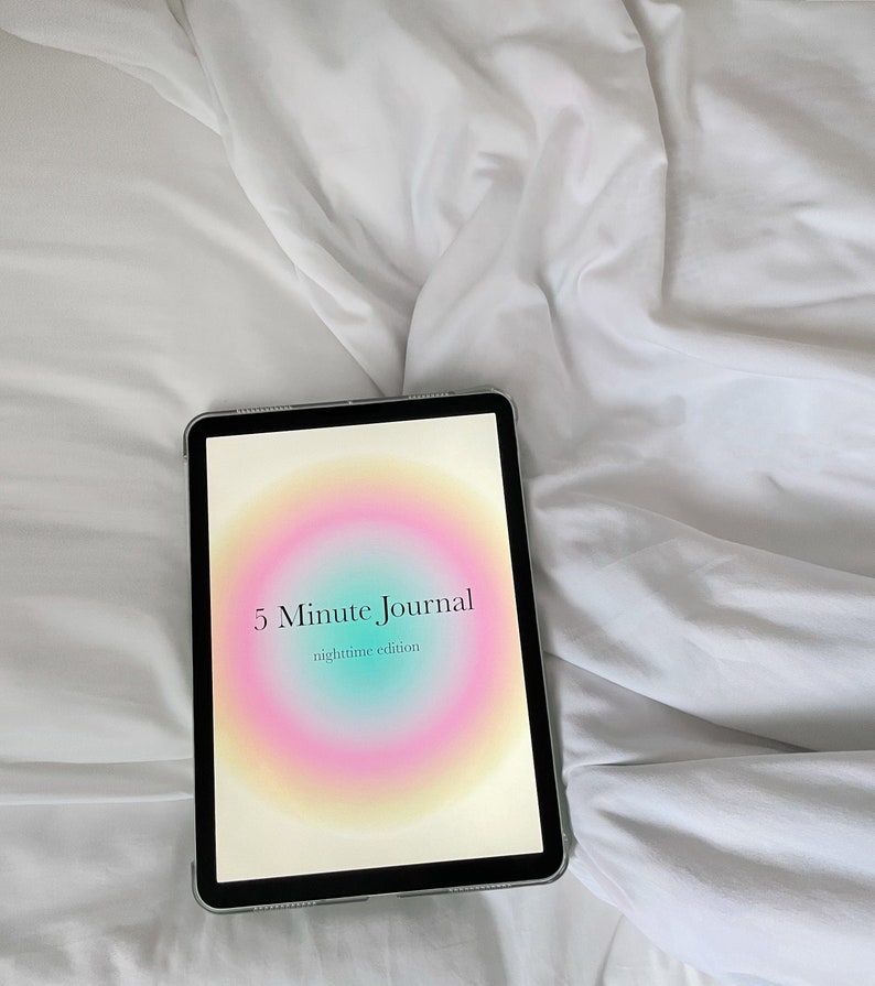 Puede incluir: Una tableta mostrando la portada de la edici&oacute;n nocturna del "5 Minute Journal". La portada presenta un c&iacute;rculo degradado de colores con el t&iacute;tulo en texto negro.