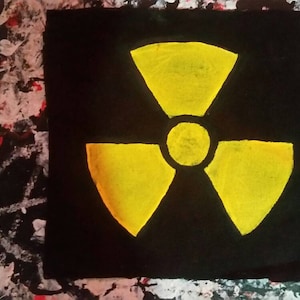 Könnte beinhalten: Ein gelbes Strahlungssymbol, das auf einen schwarzen Hintergrund gemalt ist. Das Symbol ist ein stilisiertes dreiblättriges Kleeblatt mit einem Kreis in der Mitte.