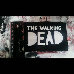 May include: A black fabric patch with the words "THE WALKING DEAD" written in white paint.