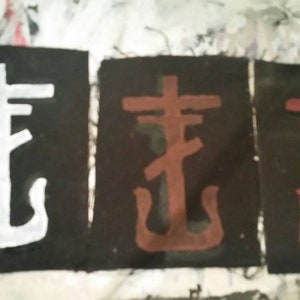 May include: Three fabric patches featuring a stylised cross and anchor design. The patches are black with white, brown, and red designs.
