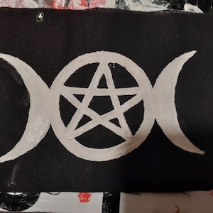 May include: A white pentacle and triple moon symbol painted on a black fabric patch.