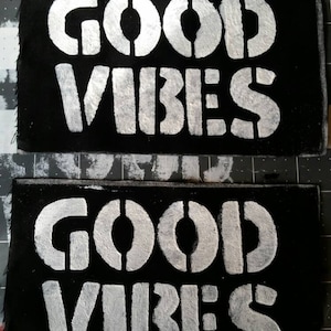 Peut inclure: Deux patchs en tissu noir avec des lettres blanches qui disent "GOOD VIBES".