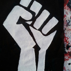 May include: A white raised fist painted on a black background. The fist is a symbol of power and solidarity.