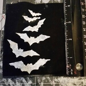 May include: A black fabric patch with five white bats of varying sizes, arranged in a vertical row, with the largest bat at the bottom.