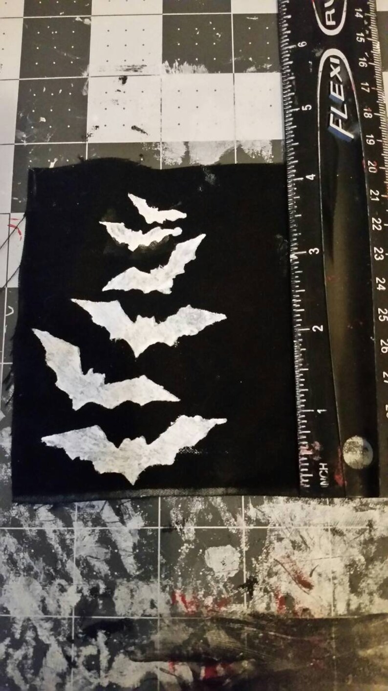 May include: A black fabric patch with five white bats of varying sizes, arranged in a vertical row, with the largest bat at the bottom.