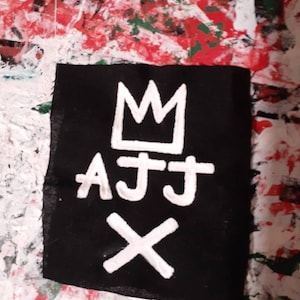 May include: Black fabric patch with white embroidered crown, letters "AJJ" and an "X".