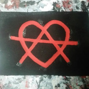 May include: A black rectangular patch featuring a red heart-shaped design intersected by a horizontal line. The heart shape is formed by a continuous line, with a small gap at the top. The background is a textured surface with splashes of white, black, and red paint.