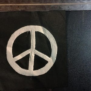 Peut inclure: Un symbole de paix blanc peint sur un carré de tissu noir. Le symbole de la paix est un cercle avec trois lignes à l'intérieur. Une règle en métal est en arrière-plan.