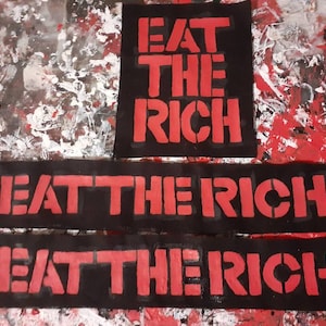 May include: Three black fabric patches with the red text "Eat the Rich" printed on them. The patches are arranged vertically, with the top patch being the smallest and the bottom patch being the largest.