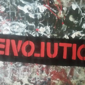 Könnte beinhalten: Ein schwarzer, rechteckiger Aufnäher mit dem Wort "REVOLUTION" in roten Buchstaben im Schablonenstil. Der Aufnäher befindet sich vor einem Hintergrund aus Farbspritzern in verschiedenen Farben, darunter Rot, Weiß und Schwarz.