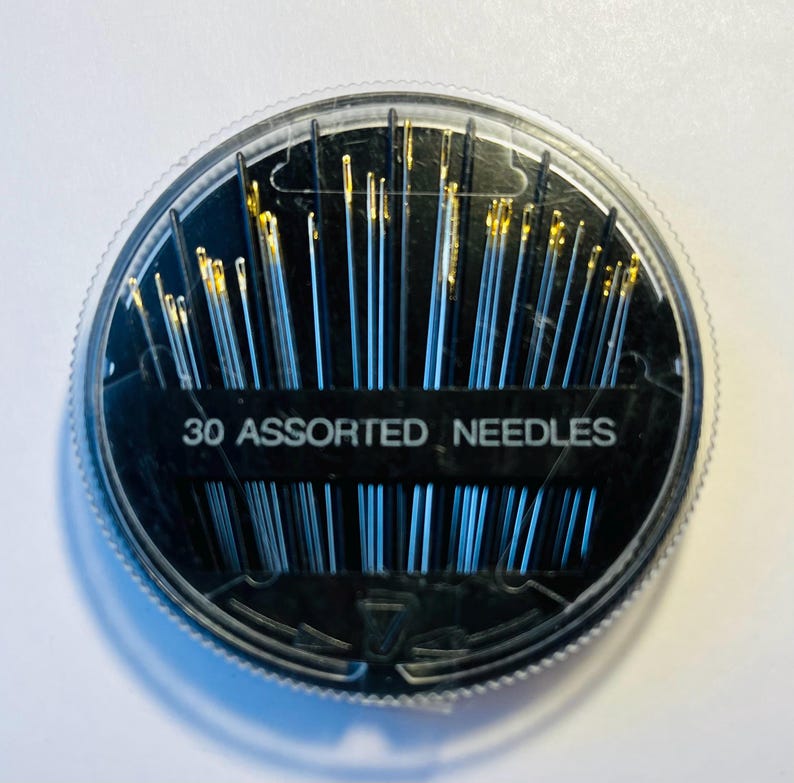 May include: A clear plastic round container with a black lid containing 30 assorted needles. The lid has the text "30 ASSORTED NEEDLES" printed on it.
