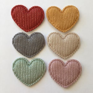 May include: Six heart-shaped fabric patches in various colours, including red, yellow, grey, green, and pink. The fabric has a corduroy texture.