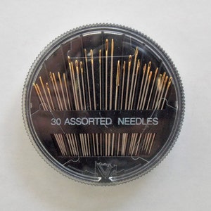 May include: A clear plastic round container with a black lid containing 30 assorted needles. The lid has the text "30 Assorted Needles" printed on it.