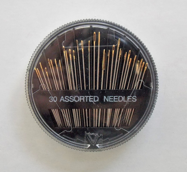 May include: A clear plastic round container with a black lid containing 30 assorted needles. The lid has the text "30 Assorted Needles" printed on it.