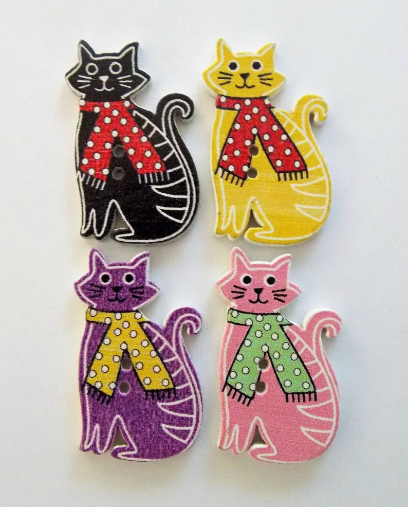 May include: Four wooden cat-shaped buttons in black, yellow, purple, and pink. Each cat wears a scarf with white polka dots. The black and yellow cats have red scarves, while the purple and pink cats have yellow and green scarves.