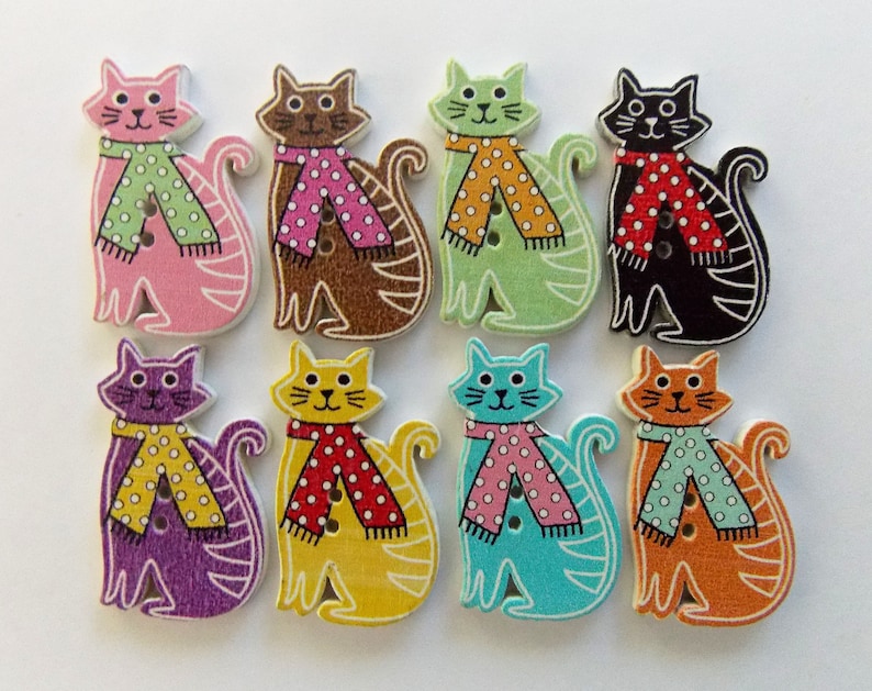 May include: A collection of eight wooden cat-shaped buttons. Each cat is painted in a different color, including pink, brown, green, black, purple, yellow, blue, and orange. The cats wear polka-dot scarves and have button closures.