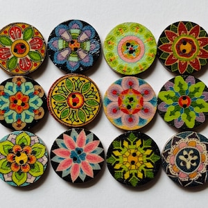 May include: Twelve round wooden buttons with floral patterns in various colours. Each button has a unique design in shades of green, blue, pink, yellow, and orange. The buttons have two or four holes for sewing and are arranged on a white surface.