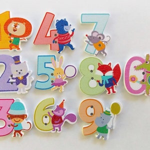 May include: A set of wooden number buttons, each adorned with a different animal character. The numbers 1 to 0 are shown, with illustrations including a lion, bear, and fox. These buttons are suitable for crafts and educational purposes.