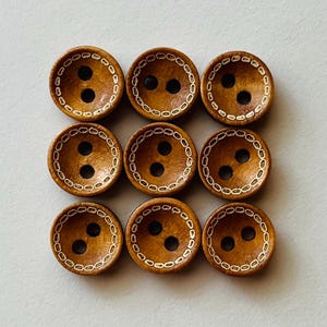 Könnte beinhalten: Neun Holzknöpfe mit jeweils zwei Löchern, angeordnet in einem Raster. Die Knöpfe haben eine warme braune Farbe mit einem weißen gepunkteten Rand. Die Knöpfe sind wahrscheinlich zum Nähen oder Basteln gedacht.
