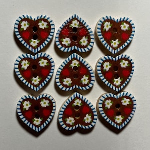 May include: Nine heart-shaped wooden buttons. Each button has a brown centre with red strawberry and white flower details. The edges are white with a blue striped border. Each button has two holes for sewing.