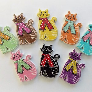 May include: A collection of nine wooden cat-shaped buttons in various colors, including green, brown, yellow, orange, pink, black, blue, and purple. Each cat wears a scarf with a polka dot pattern. The buttons have two holes for sewing.