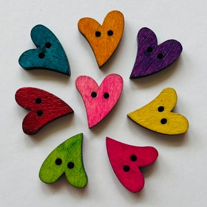 May include: Eight wooden heart-shaped buttons in various colours, including red, pink, yellow, green, blue, and purple. Each button has two black holes for sewing.