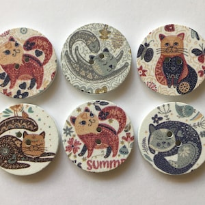 May include: Six round wooden buttons with colourful cat designs. The buttons feature various cat poses, including a cat curled up, a cat sitting, and a cat standing. The buttons are decorated with floral patterns and other details.