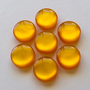 Può includere: Sette cabochon rotondi in vetro giallo con una superficie lucida e riflettente.