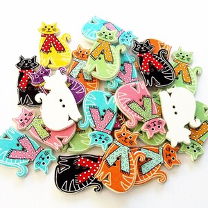May include: A collection of colorful wooden cat-shaped buttons. The buttons feature various colors, including yellow, black, orange, and green, with patterned scarves and polka dots. Some buttons have two holes for sewing.