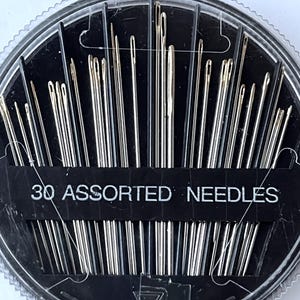 May include: A clear plastic round container with a black lid holds 30 assorted needles. The container has a black label that reads "30 Assorted Needles".