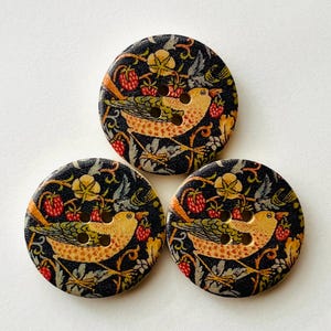May include: Three round buttons featuring a dark background with a repeating pattern of yellow birds, red strawberries, and green foliage. Each button has four holes in the centre for attachment, arranged in a square formation on the surface.
