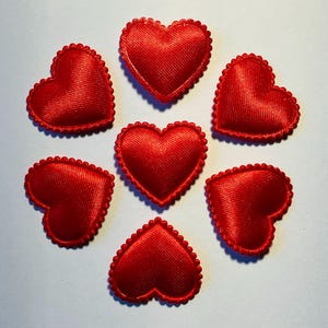 May include: Seven red heart-shaped fabric appliques. Each heart has a scalloped edge and a satin-like texture. The hearts are arranged in a circular pattern against a white background, creating a romantic theme.
