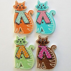 May include: Four wooden cat-shaped buttons in orange, turquoise, green, and brown. Each cat wears a scarf with polka dots. The buttons have a white outline and are suitable for sewing or crafting projects.