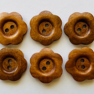 May include: Six brown wooden flower-shaped buttons with two holes each.
