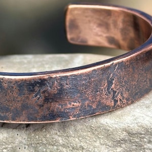 May include: A wide copper bracelet with a hammered finish. The bracelet has a rustic, aged look.