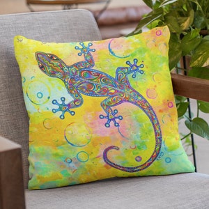 May include: A colorful throw pillow with a yellow background and a blue, green, and purple gecko with a swirling pattern. The gecko is surrounded by white circles.