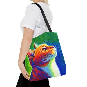 May include: A tote bag with a colorful illustration of a cat looking up. The cat is orange, white, and has a rainbow-like effect. The background is a green and blue gradient.