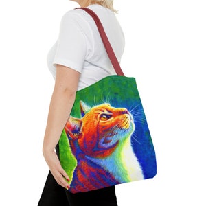 May include: A tote bag with a colorful illustration of a cat looking up. The cat is orange, white, and has a rainbow-like effect. The background is a green and blue gradient.