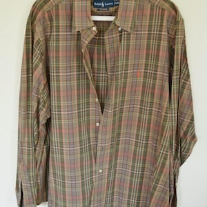 May include: A long-sleeved plaid shirt in shades of olive green, pink, and blue, hanging on a white hanger. The shirt has a button-down front and a small red logo on the chest. The label reads "Ralph Lauren Classic Fit."