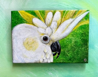 Cacatúa de 10.75''x7.3''x1/4'', blanca con cresta amarilla, fondo verde, pintada con acrílico sobre masonite.