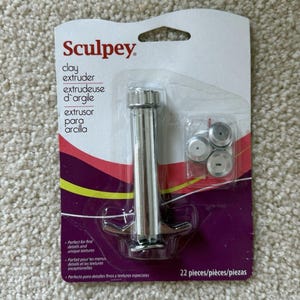 May include: A silver-colored clay extruder tool with multiple interchangeable tips, packaged on a purple and white card. The package includes the brand name "Sculpey" and the text "clay extruder". The package contains 22 pieces.