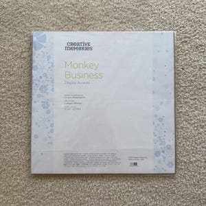 May include: A package of Creative Memories "Monkey Business" display accents. The package is white with a light blue floral design and the words "Monkey Business" in green. The package also includes text in French, German, and Japanese.